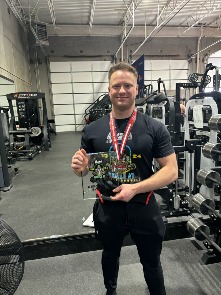 Daniel standing in a gym holding a plaque and wearing a medal.